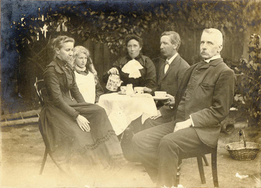 Four adults and one child sit at a table in the garden having tea