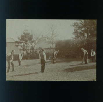 Six late teenage boys playing cricket next to the fence at RVIB