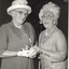 Two ladies in hats speaking at a function (Augusta on right)