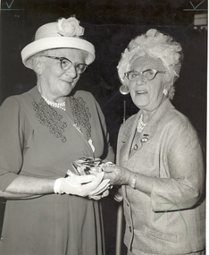 Two ladies in hats speaking at a function (Augusta on right)