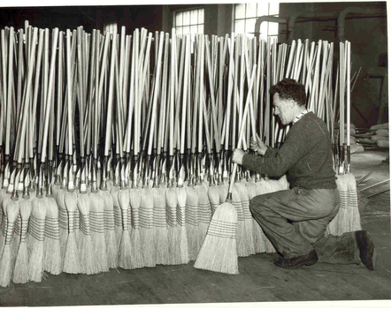 Man kneeling as he stacks completed brooms