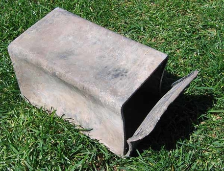 Metal box sits on grass, with one end sawn off