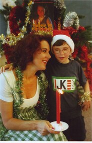 Rhonda kneels, holding a red candle with an arm around a boy wearing a Santa hat
