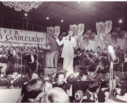 Mark Holden smiling as he croons on stage in a white suit