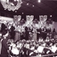 Four couples sing awkwardly on stage with Harold Badger and Bruce Mansfield
