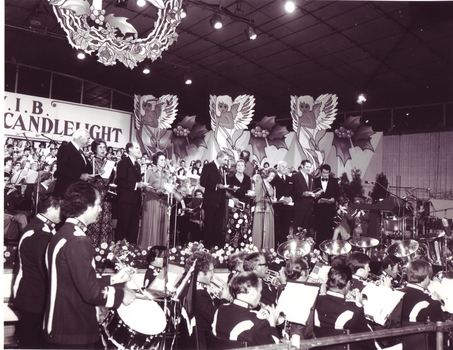 Four couples sing awkwardly on stage with Harold Badger and Bruce Mansfield
