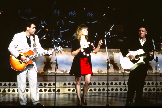 A three piece band, two guitarists and one singer, play on stage