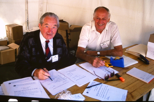 Two volunteers with various forms and boxes around them