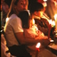 Woman holding young girl on her lap amongst candlelight crowd
