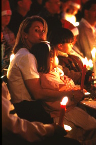 Woman holding young girl on her lap amongst candlelight crowd