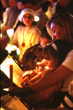 Woman holding young girl on her lap amongst candlelight crowd
