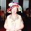 Woman wearing a hat with skeins of yarn and knitting needles on top, holding flowers