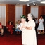 A nursing sister helps an older woman wearing a green spikey hat with tinsel across the floor