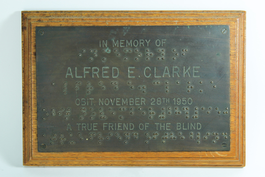 Metal plate with text and Braille, attached to wooden plaque
