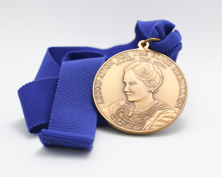 Bronze coloured medallion with writing and image of Tilly Aston on blue ribbed ribbon