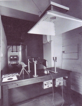 Behind shooting table with rifle in frame and target down narrow corridor