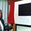Man in suit with gold chain holding draw cord that revealed plaque