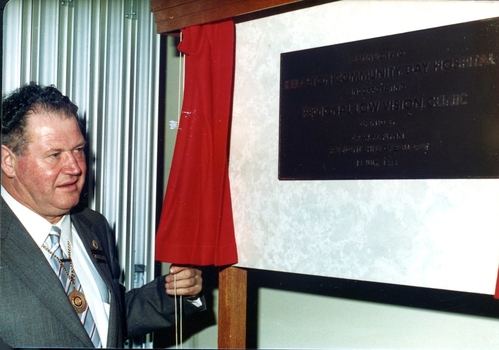 Man in suit with gold chain holding draw cord that revealed plaque