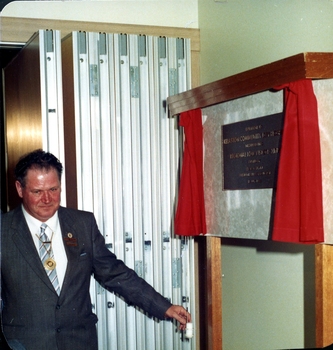 Man in suit with gold chain of office holding draw cord that revealed plaque