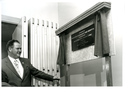 Man in suit with gold chain holding draw cord that revealed plaque