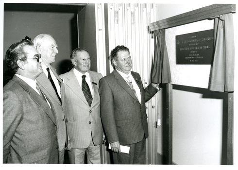 Four men in suits looking at plaque