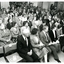 People in rows of seats and standing behind them in a large room