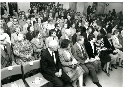 People in rows of seats and standing behind them in a large room