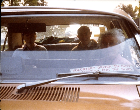 Three people sit in a car driven by a volunteer