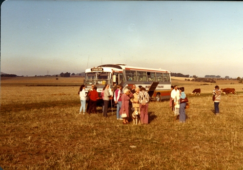 Group of people standing next to a bus in a field