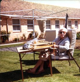Seated woman with a weaving frame outside