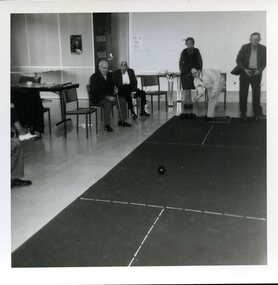 Group of players around an indoor bowling green watching a bowl