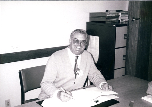 Man smiling as he sits behind a desk, looking at reports