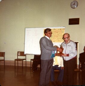 Man handing a trophy to another during a presentation