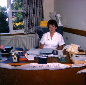 Woman in white nursing uniform sits at a desk