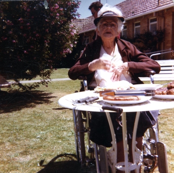 Older woman in wheelchair sits at garden table