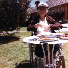 Older woman in wheelchair sits at garden table