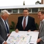 Three men in carpark holding design sketch of updated building