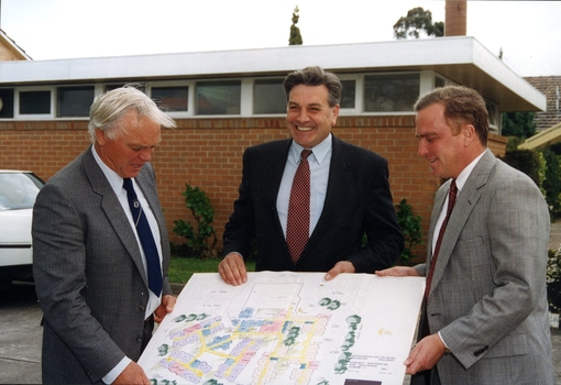 Three men in carpark holding design sketch of updated building