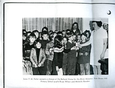 Nurse receives cheque from girl and boy primary school pupils, whilst classmates look on