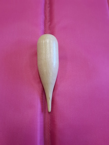 Polished milk coloured wooden shape cylindrical one end, conical tapering other end, coming to a blunted point-single point. 