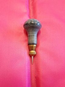 Braille stylus consisting of varnished wooden handle and metal pointed end.