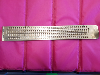 Two metal plates with hinge on right and openings for 4 lines of Braille