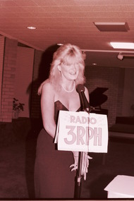 Blonde haired woman behind microphone in evening dress