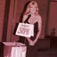 Blonde haired woman behind microphone in evening dress