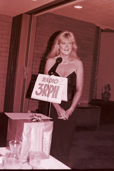 Blonde haired woman behind microphone in evening dress