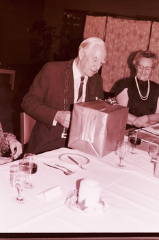 John Wicking looking at his wrapped gift, with Eunice Wilson looking on