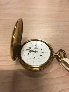Gold coloured watch case with white clock face and Braille markings