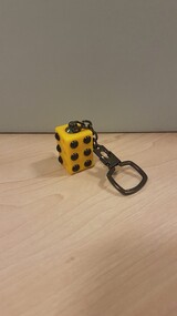 Yellow cuboid with raised circles on each long side attached to a chain