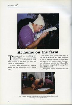 Michael Fazio looking at a magazine close to his face.  Michael uses a magnifier whilst wife Therese watches at the kitchen table.