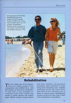 A man holding a white cane walks along a beach whilst holding the arm of a female.